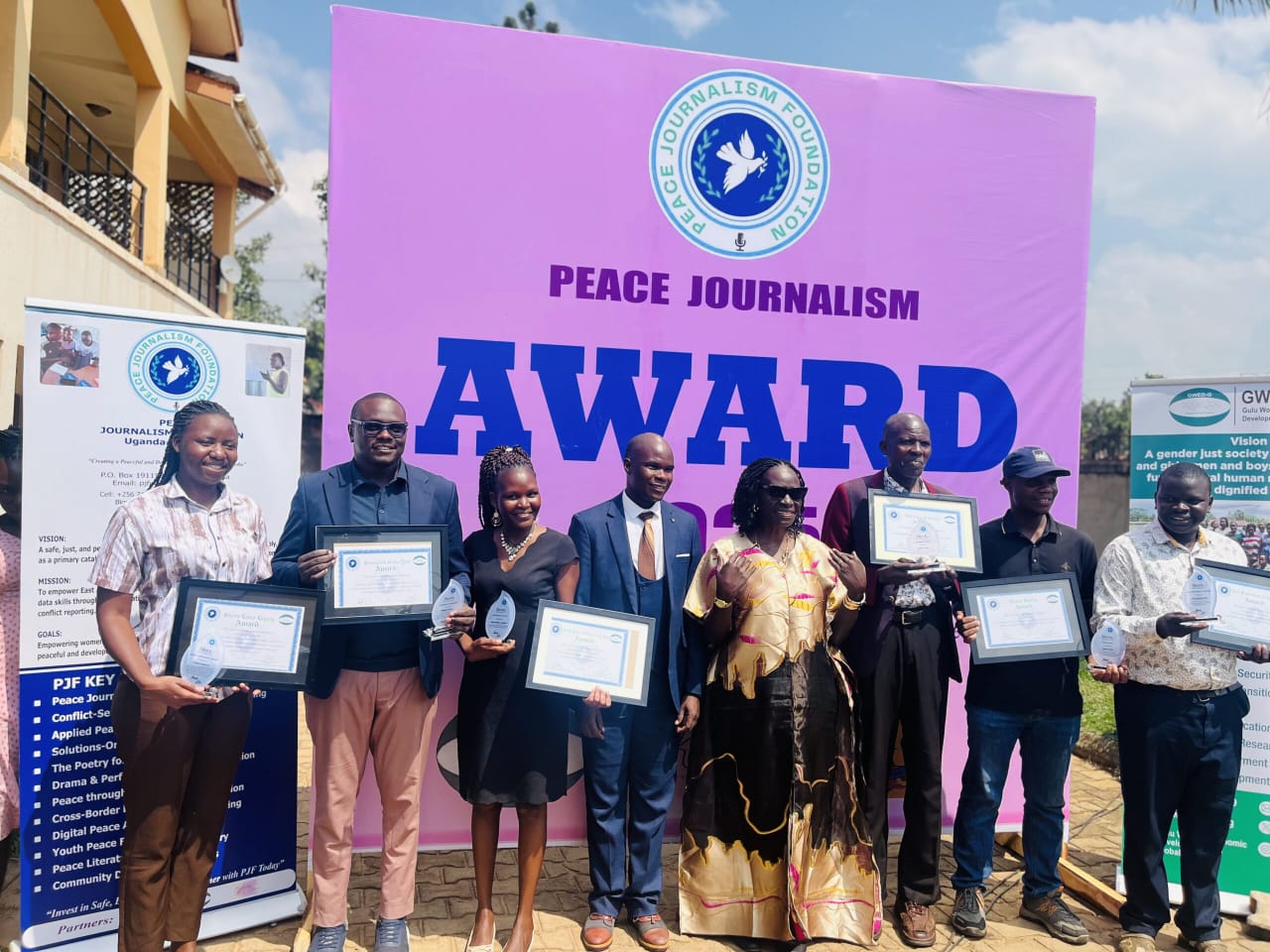 The 2025 award winners holding their certificates and trophies in front of the Peace Journalism Award banner